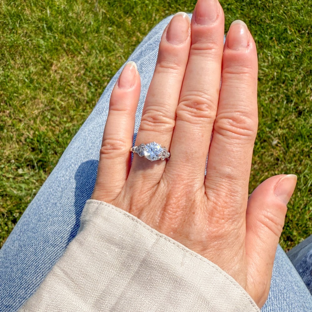 A 1930s platinum engagement ring featuring a central round old cut diamond with geometric accent-set shoulders. View VI