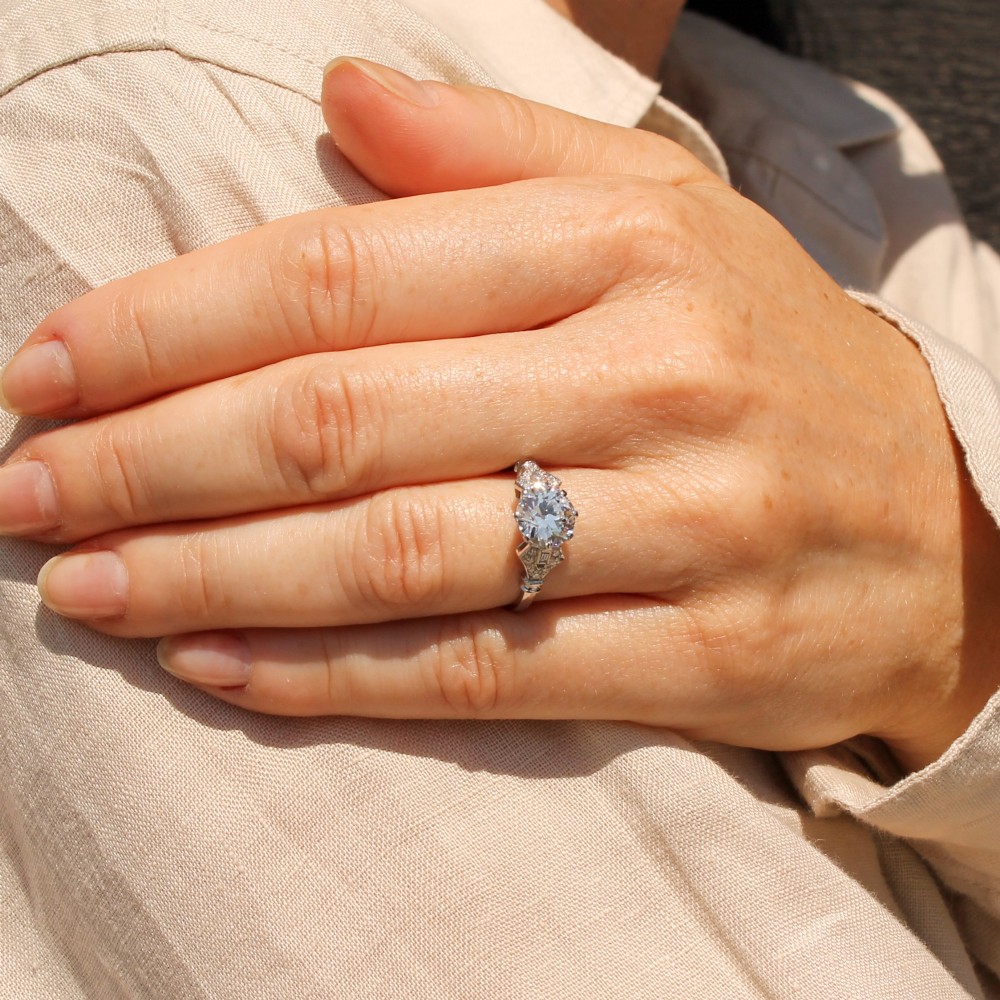 A 1930s platinum engagement ring featuring a central round old cut diamond with geometric accent-set shoulders. View VII