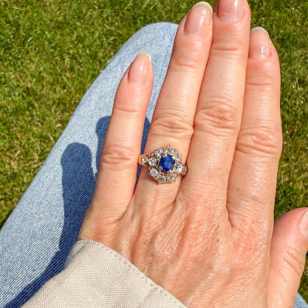 An antique yellow gold ring featuring a central cushion-cut blue sapphire surrounded by a halo of old cut diamonds. View II