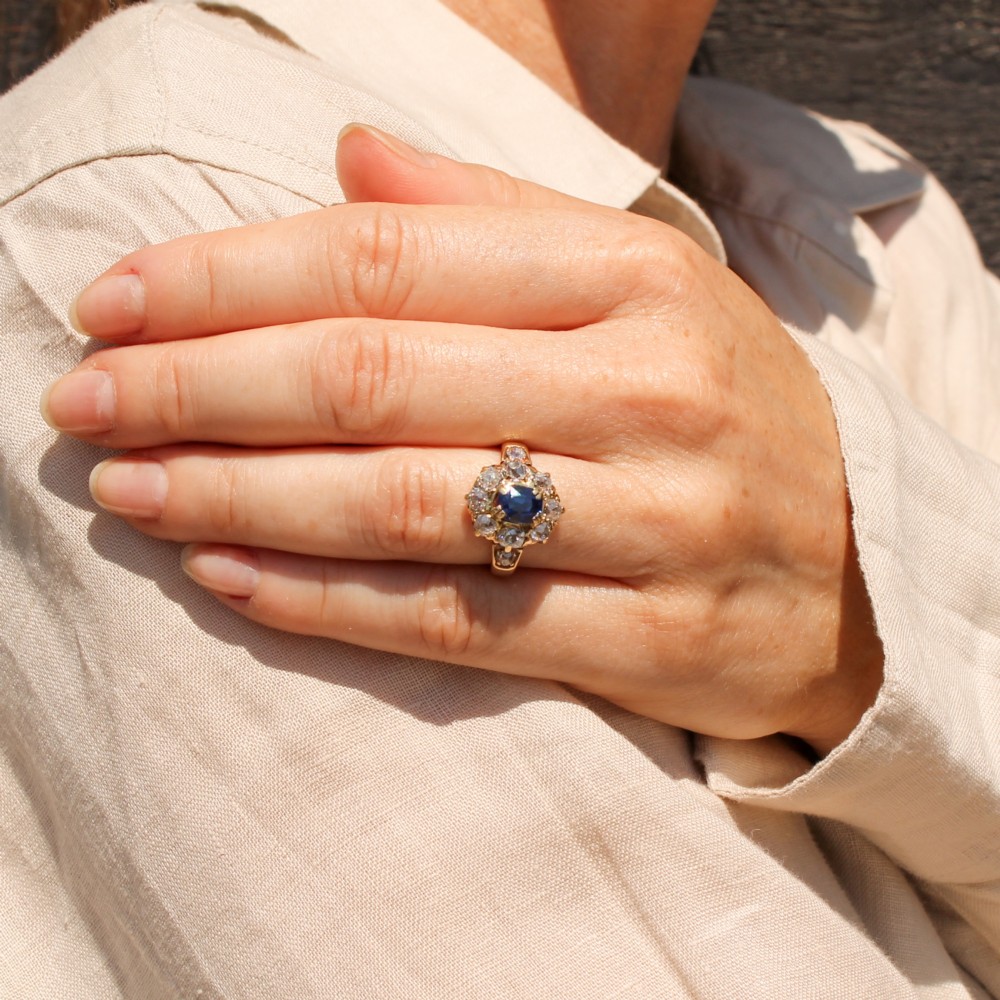 An antique yellow gold ring featuring a central cushion-cut blue sapphire surrounded by a halo of old cut diamonds. View VII