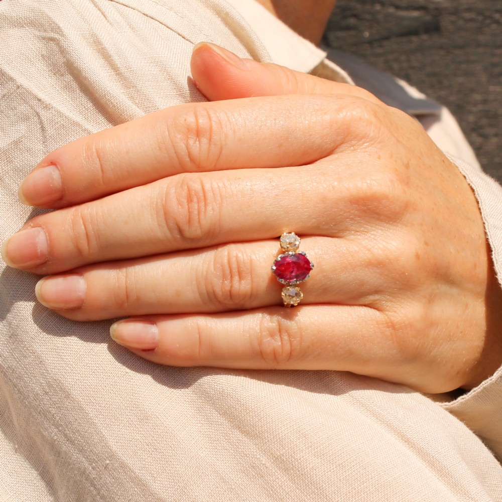 An antique yellow gold ring set with a central oval pinkish-red ruby flanked by two round old cut diamonds in claw settings. View II