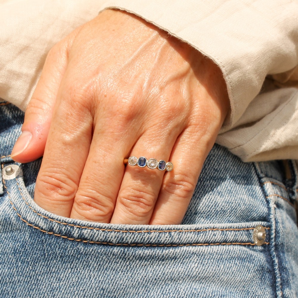 An antique yellow gold ring set with five alternating old cut diamonds and cushion-shaped blue sapphires featuring millegrain details. View II