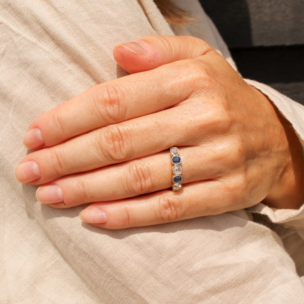 An antique yellow gold ring set with five alternating old cut diamonds and cushion-shaped blue sapphires featuring millegrain details. View VI