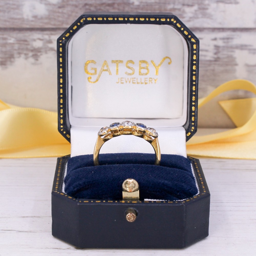 An antique yellow gold ring set with five alternating old cut diamonds and cushion-shaped blue sapphires featuring millegrain details. View IX
