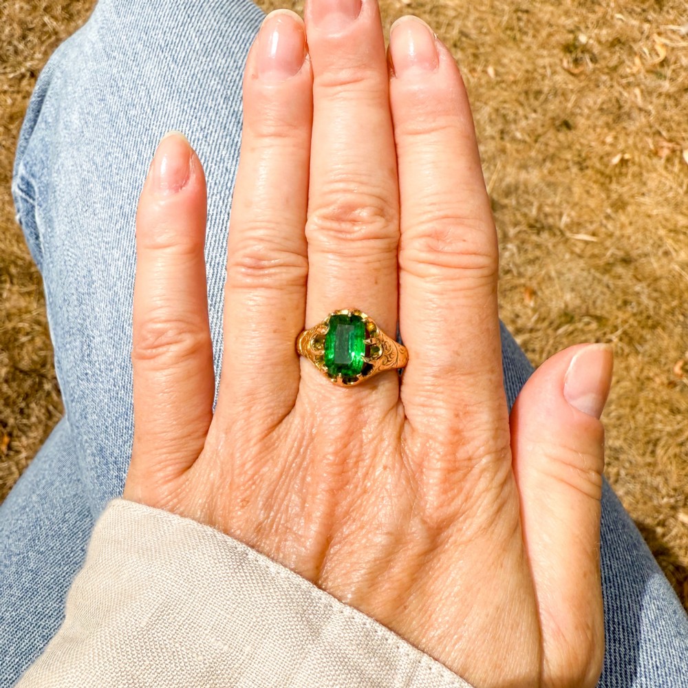 An antique gold ring featuring a cushion-cut green tsavorite garnet held in multi-claw settings with scroll-engraved shoulders. View VII