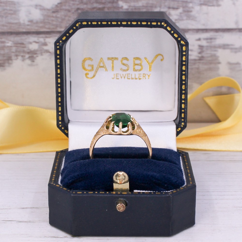 An antique gold ring featuring a cushion-cut green tsavorite garnet held in multi-claw settings with scroll-engraved shoulders. View IX