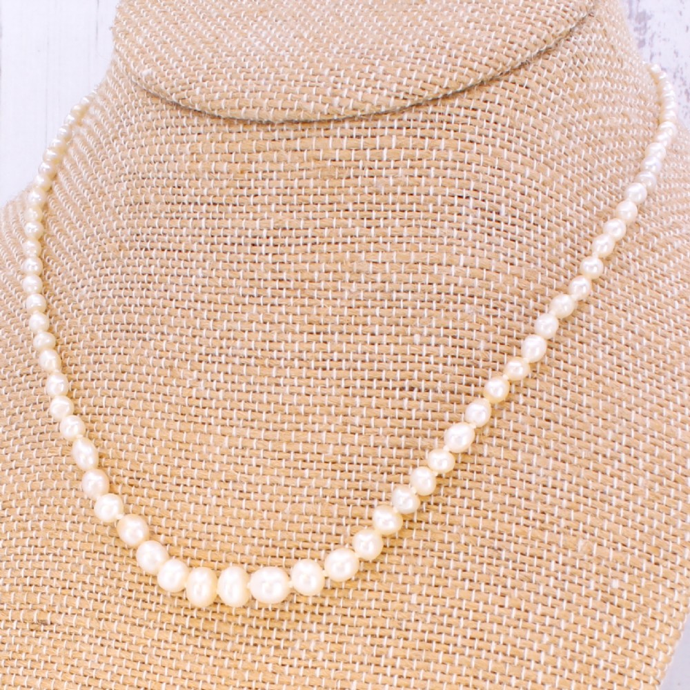 A single strand of vintage graduated cream saltwater pearls display strung on a neck display bust.