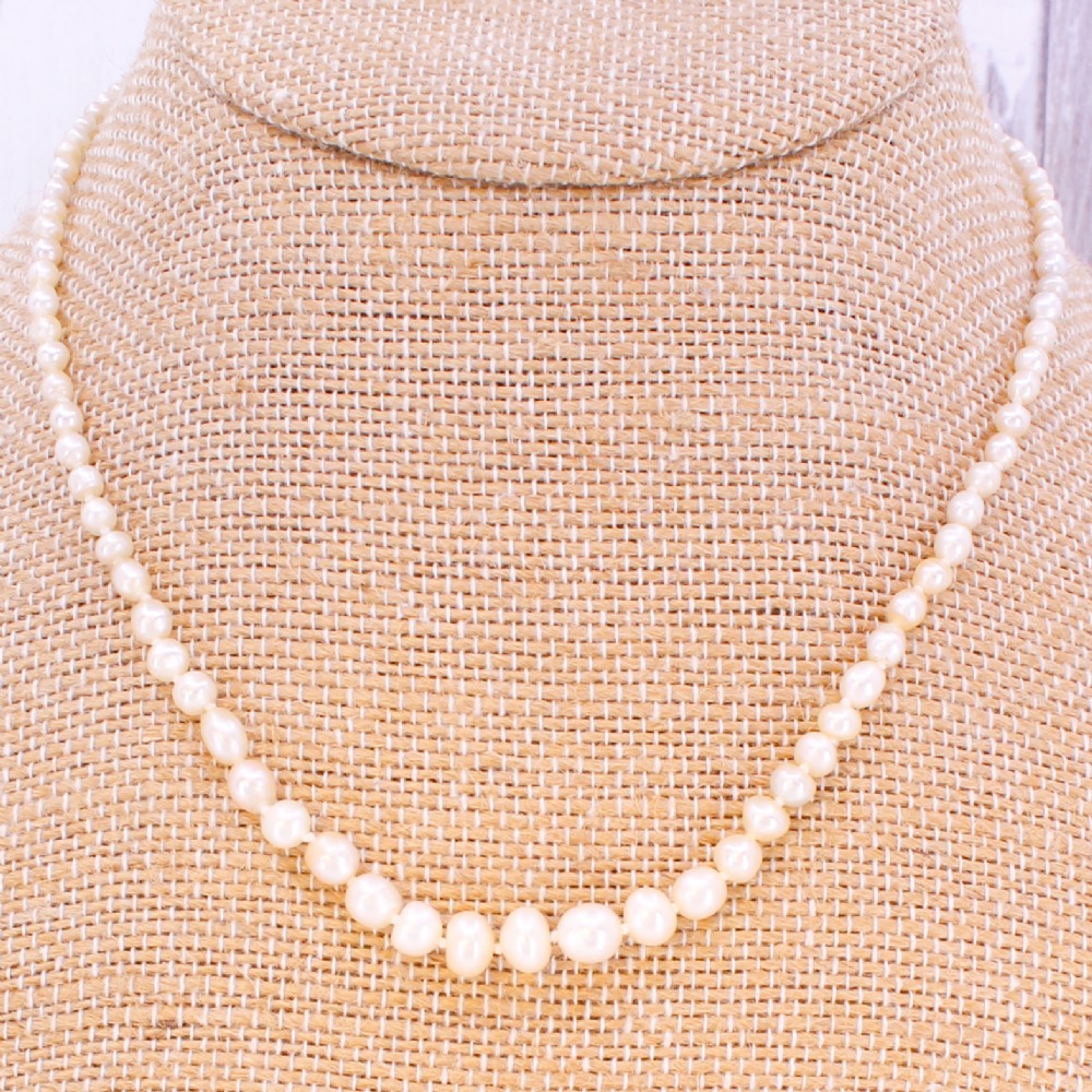 A single strand of vintage graduated cream saltwater pearls display strung on a neck display bust. View III