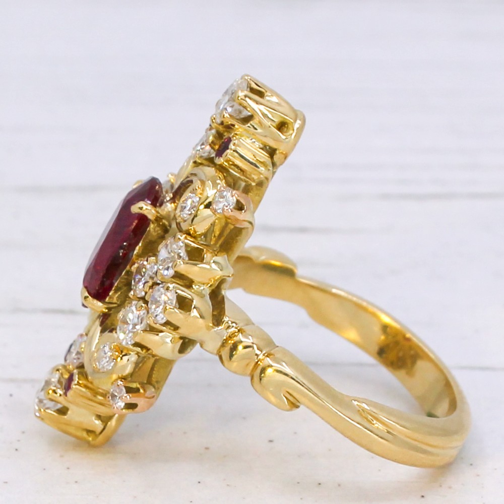 A yellow gold vintage ring featuring an oval red ruby surrounded by openwork scroll motifs set with round diamonds and accent rubies. View IV