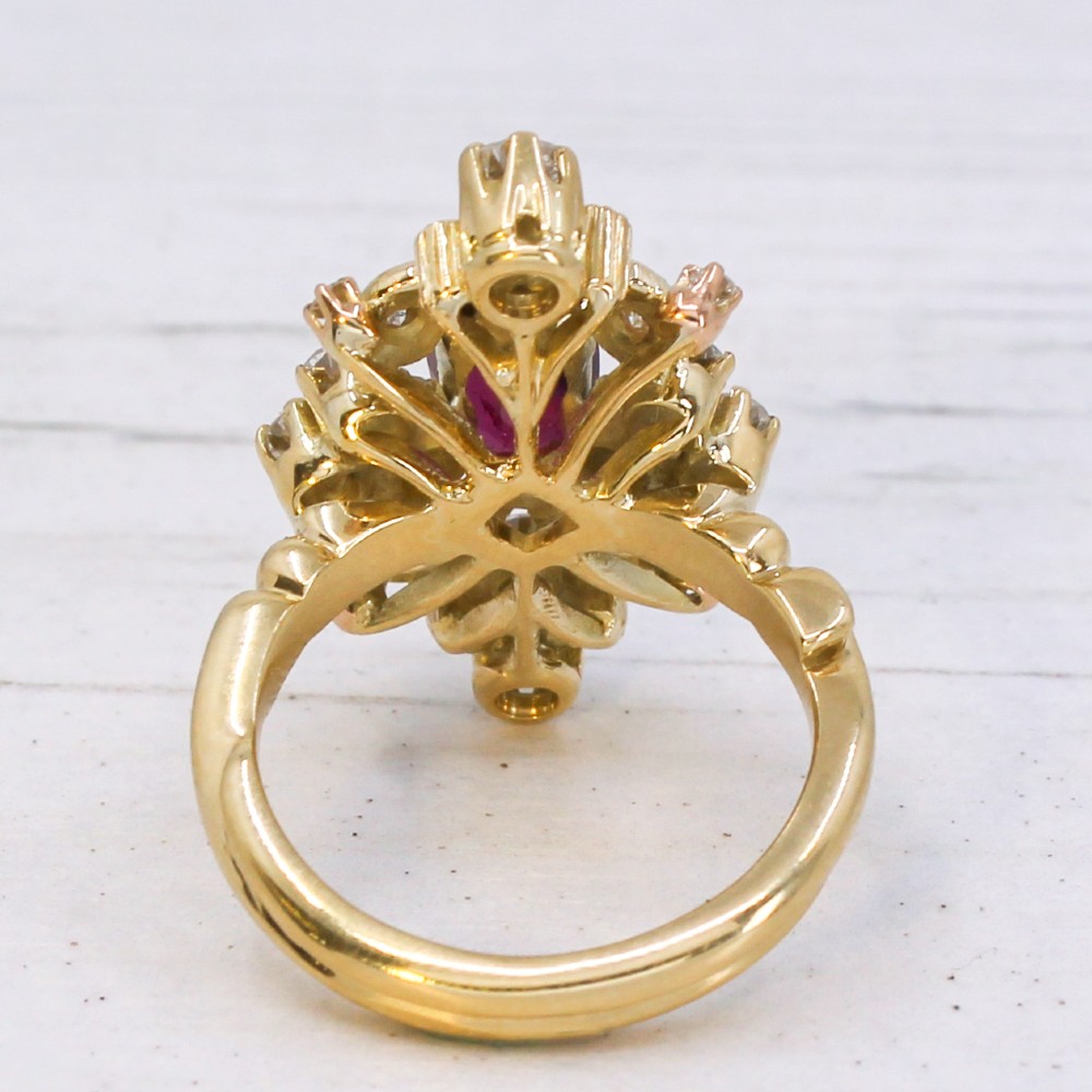 A yellow gold vintage ring featuring an oval red ruby surrounded by openwork scroll motifs set with round diamonds and accent rubies. View V