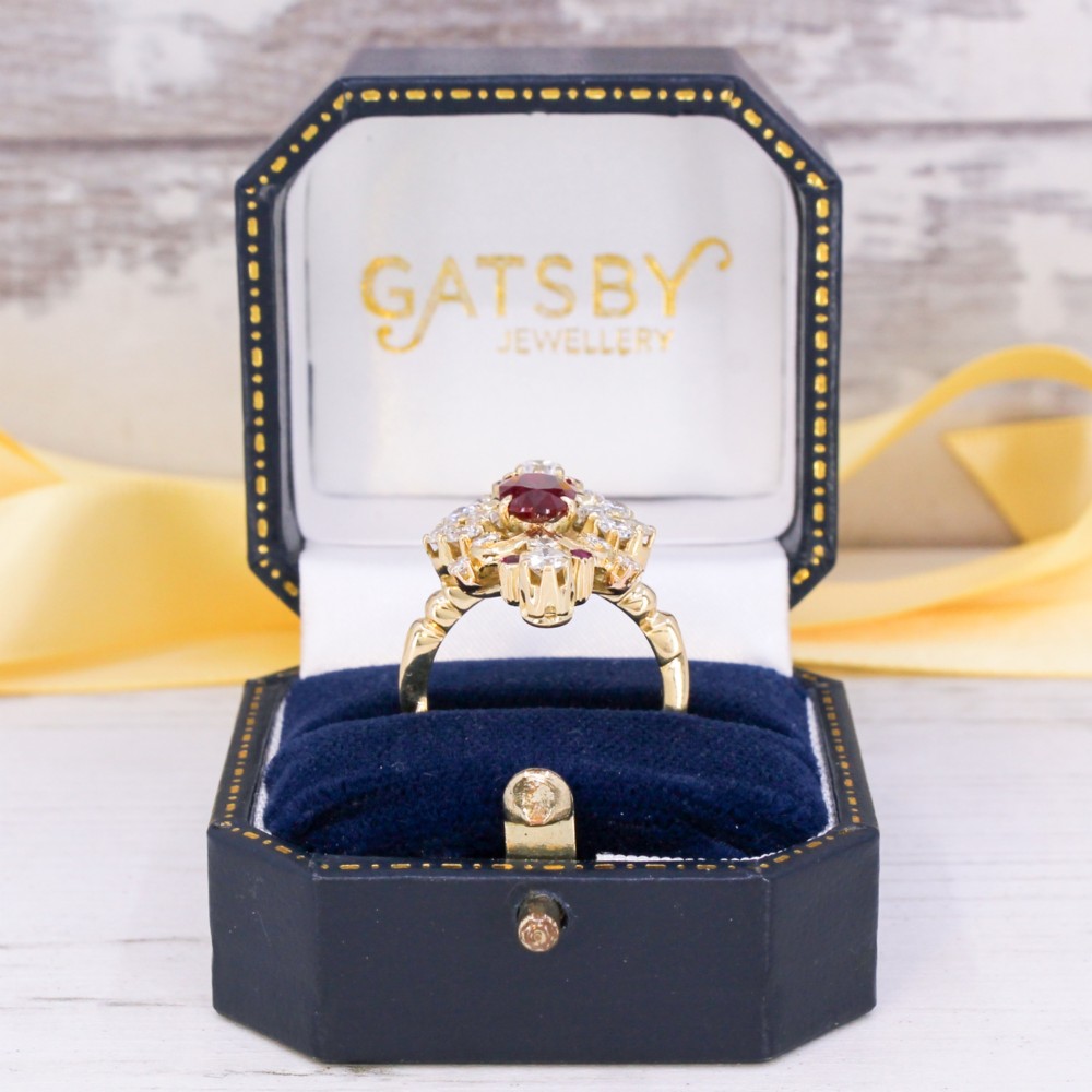 A yellow gold vintage ring featuring an oval red ruby surrounded by openwork scroll motifs set with round diamonds and accent rubies. View IX