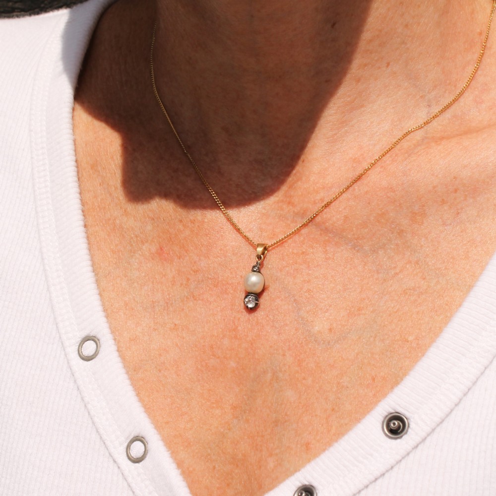 An antique gold chain holding a vertical drop pendant featuring a natural pearl suspended between two bezel-set diamonds. View II