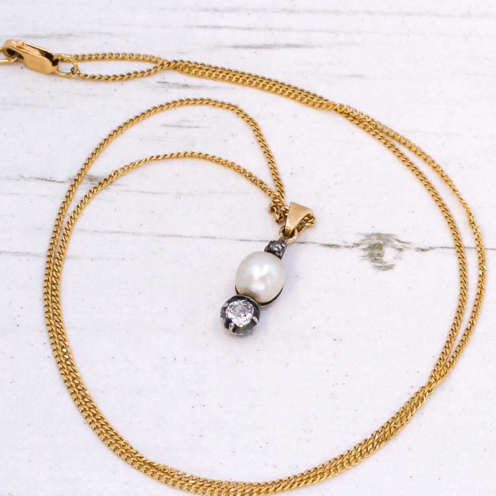 An antique gold chain holding a vertical drop pendant featuring a natural pearl suspended between two bezel-set diamonds. View V
