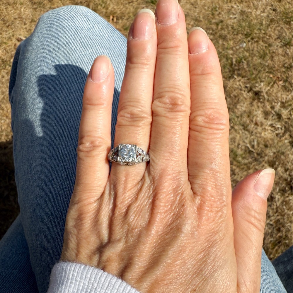 An Art Deco platinum engagement ring featuring a central old European cut diamond set within intricate pierced filigree shoulders. View VI