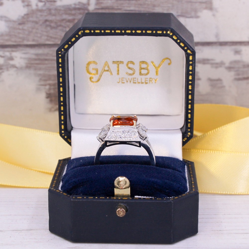 A mid-century vintage cocktail ring featuring a cushion-cut orange garnet central gemstone flanked by pave and marquise diamond accents set in a white gold band. View IX