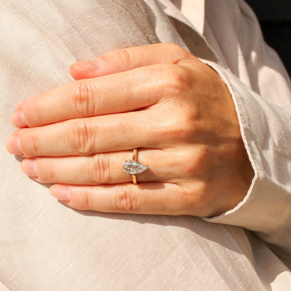 A vintage solitaire ring featuring a pear-cut diamond held in white metal claw settings on a smooth yellow gold band. View VI