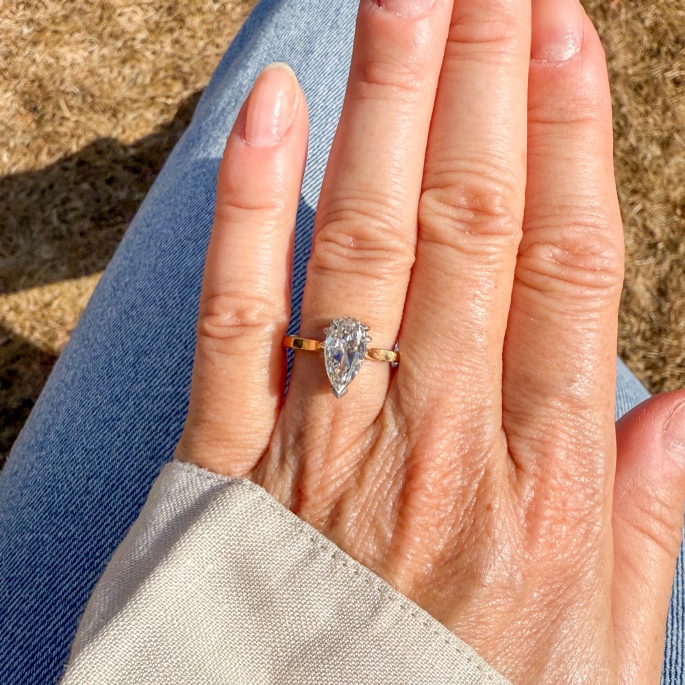 A vintage solitaire ring featuring a pear-cut diamond held in white metal claw settings on a smooth yellow gold band. View VII