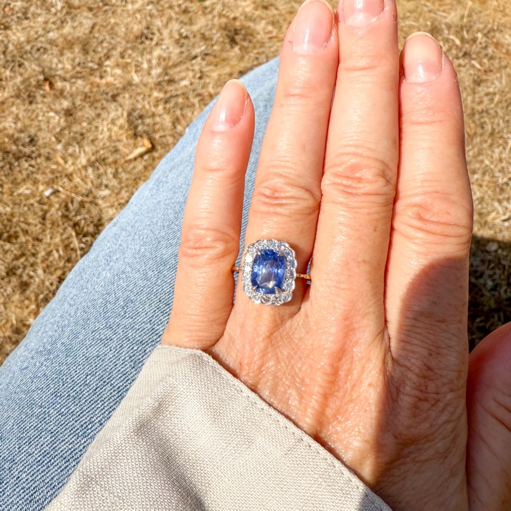 A cushion-cut blue Ceylon sapphire set in a multi-claw setting surrounded by a halo of brilliant white diamonds on a yellow gold band. View VI