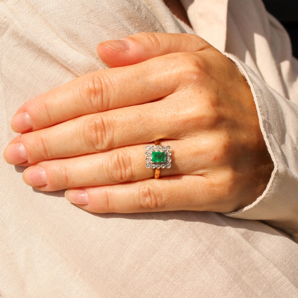 An antique yellow gold ring set with a rectangular central green emerald surrounded by a scalloped halo of small old cut diamonds. View II