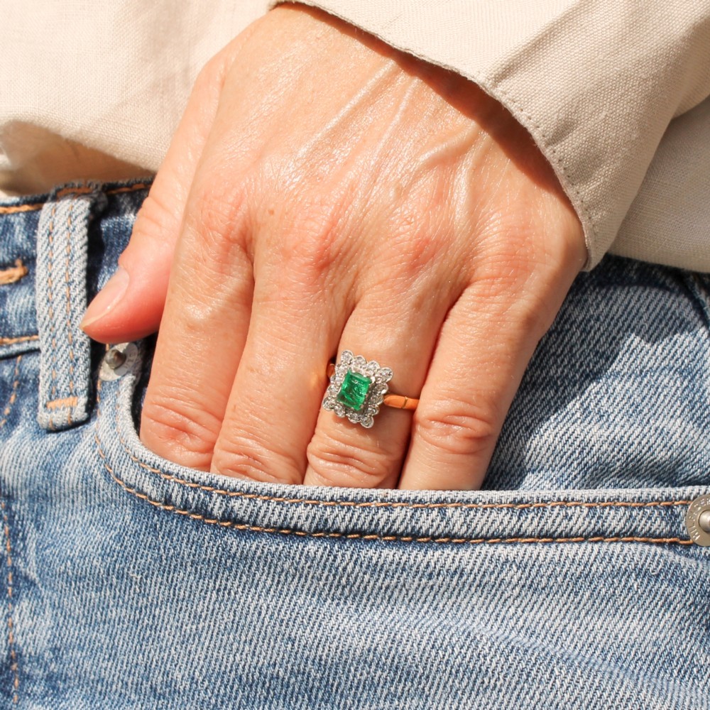 An antique yellow gold ring set with a rectangular central green emerald surrounded by a scalloped halo of small old cut diamonds. View VI
