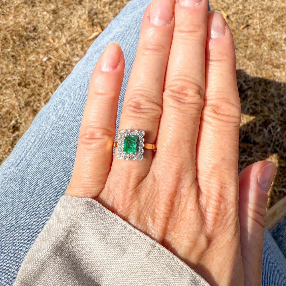 An antique yellow gold ring set with a rectangular central green emerald surrounded by a scalloped halo of small old cut diamonds. View VII