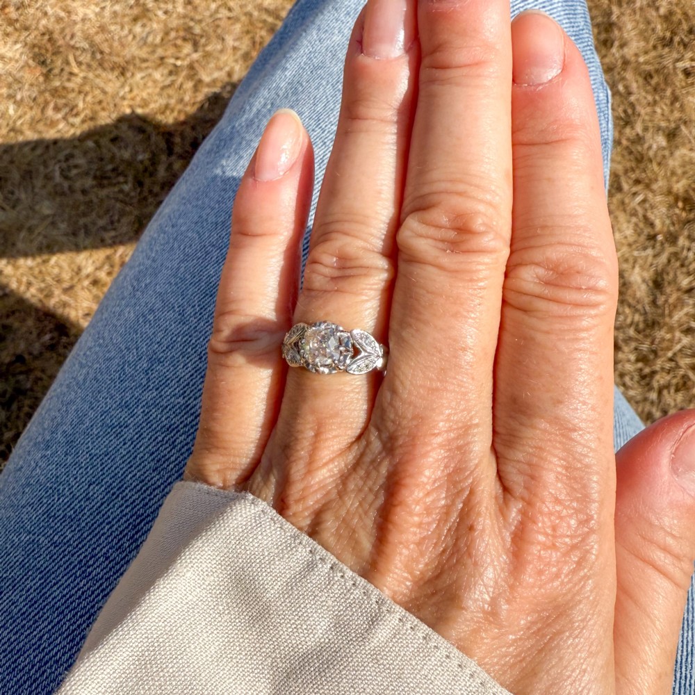 An Art Deco diamond ring featuring a central old cut diamond set in platinum with leaf-motif shoulders on an 18ct yellow gold band. View VI