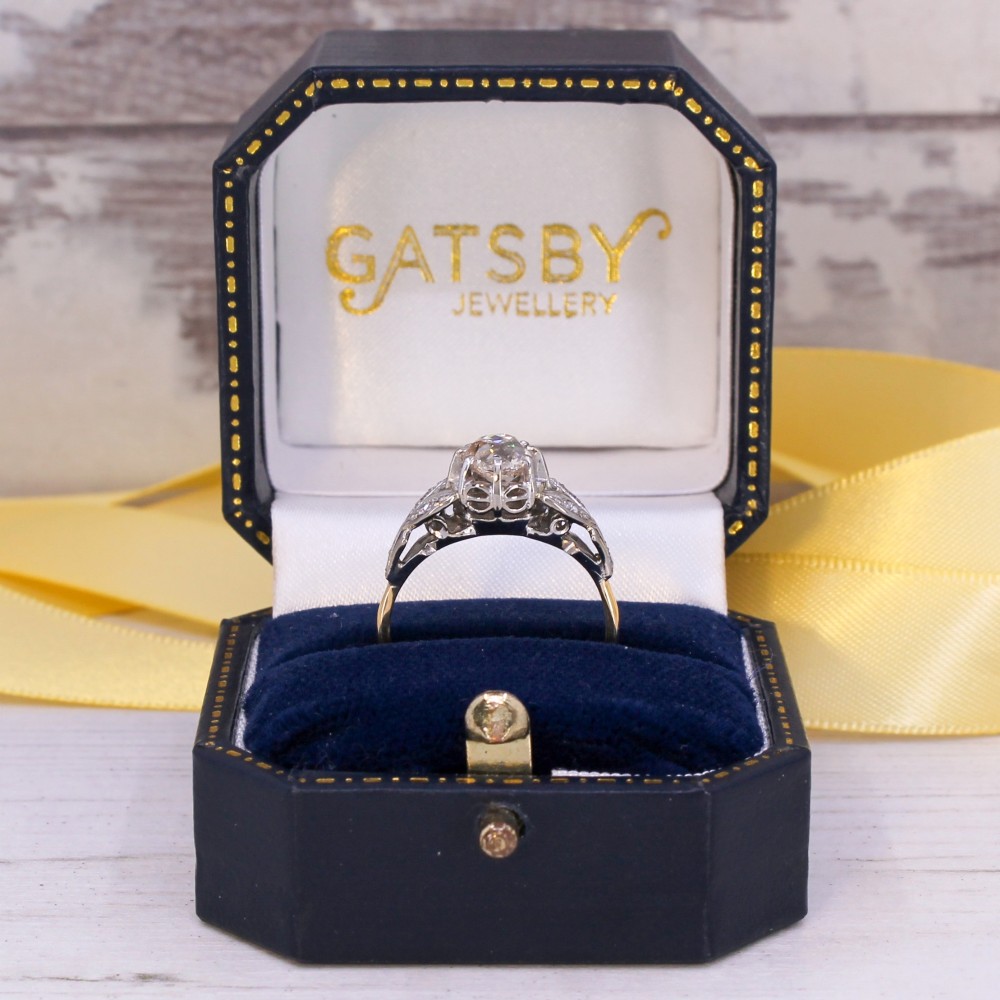 An Art Deco diamond ring featuring a central old cut diamond set in platinum with leaf-motif shoulders on an 18ct yellow gold band. View IX