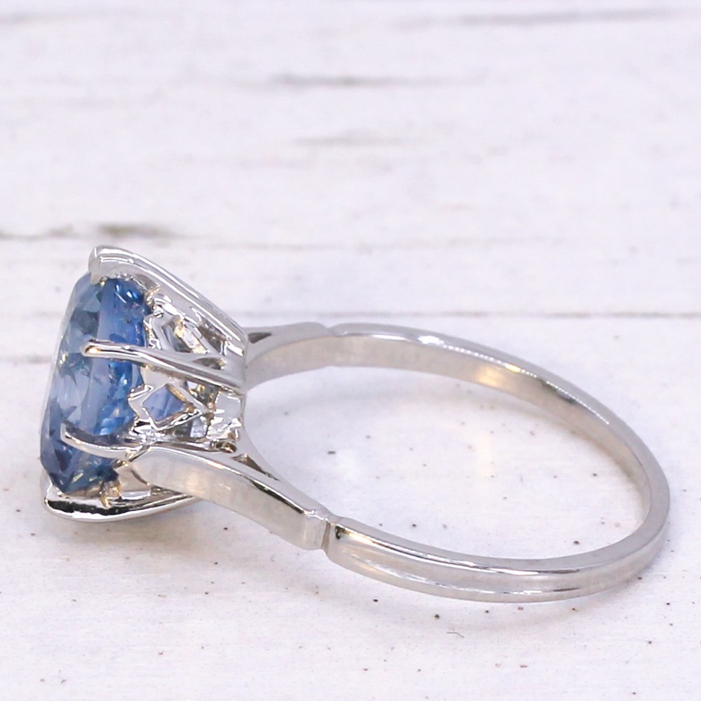 An Art Deco platinum solitaire ring featuring a large oval-cut light blue sapphire held in an eight-claw setting. View IV