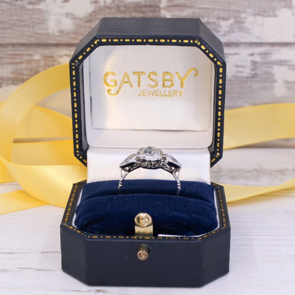 An Art Deco platinum ring featuring a central bezel-set old cushion-cut diamond flanked by two pear-cut side diamonds with milgrain edging. View IX