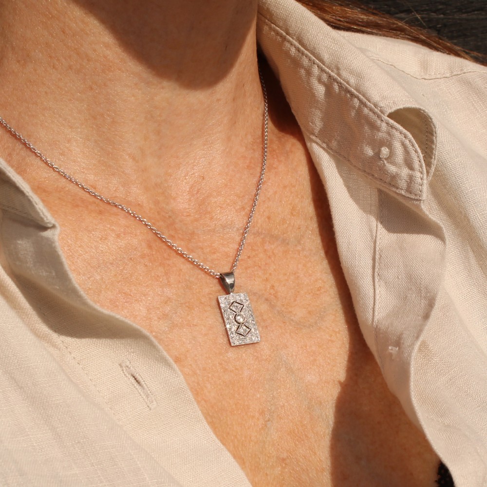 A rectangular Art Deco pendant set with a central round old cut diamond within a geometric diamond-paved frame on a silver chain. View II