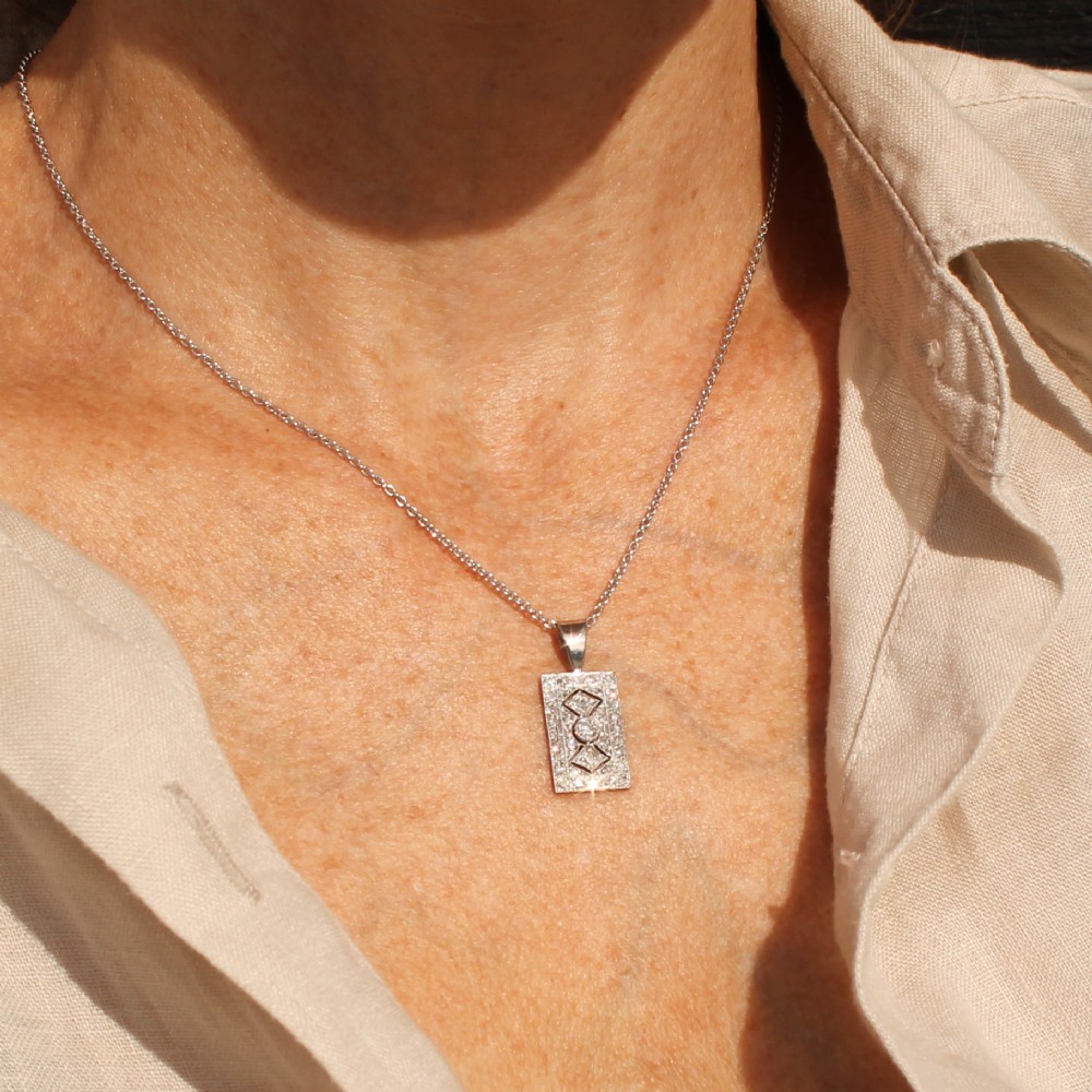 A rectangular Art Deco pendant set with a central round old cut diamond within a geometric diamond-paved frame on a silver chain. View III
