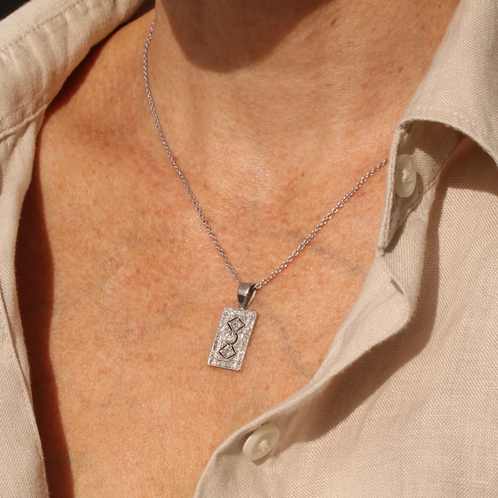 A rectangular Art Deco pendant set with a central round old cut diamond within a geometric diamond-paved frame on a silver chain. View V