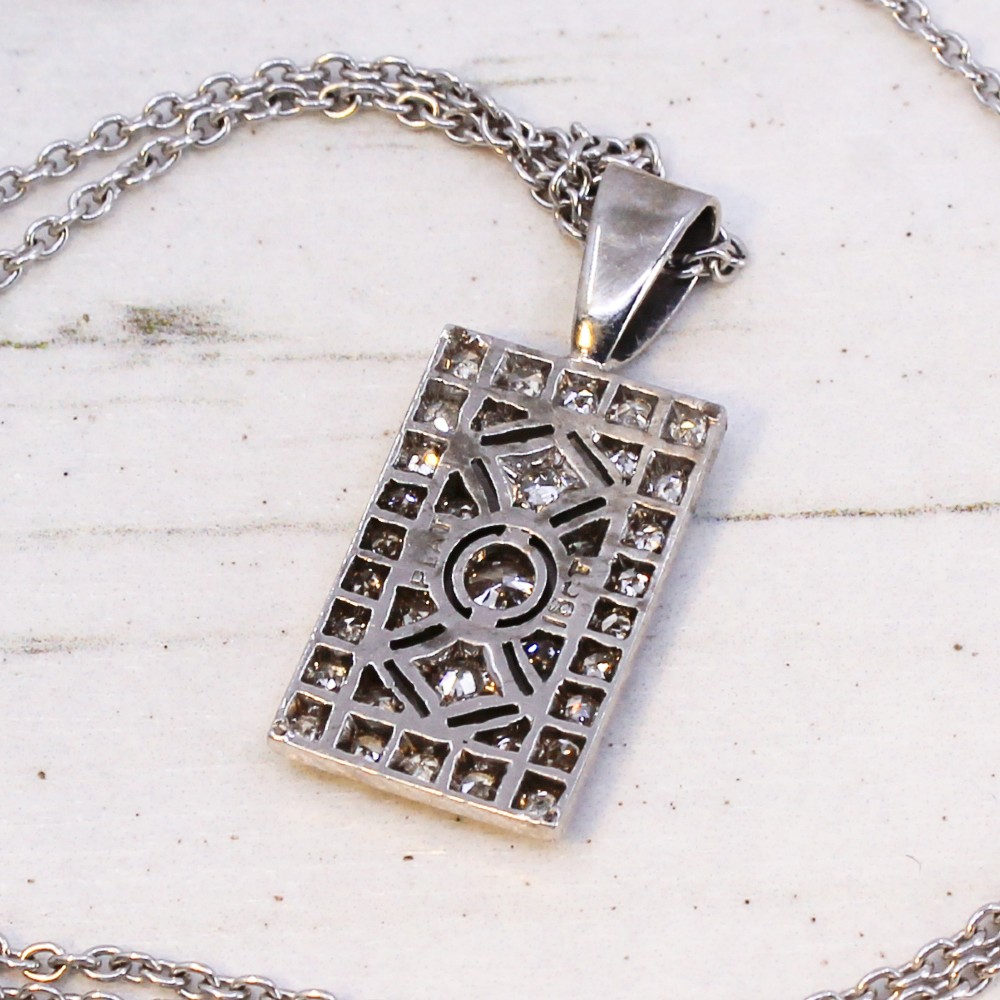 A rectangular Art Deco pendant set with a central round old cut diamond within a geometric diamond-paved frame on a silver chain. View VI