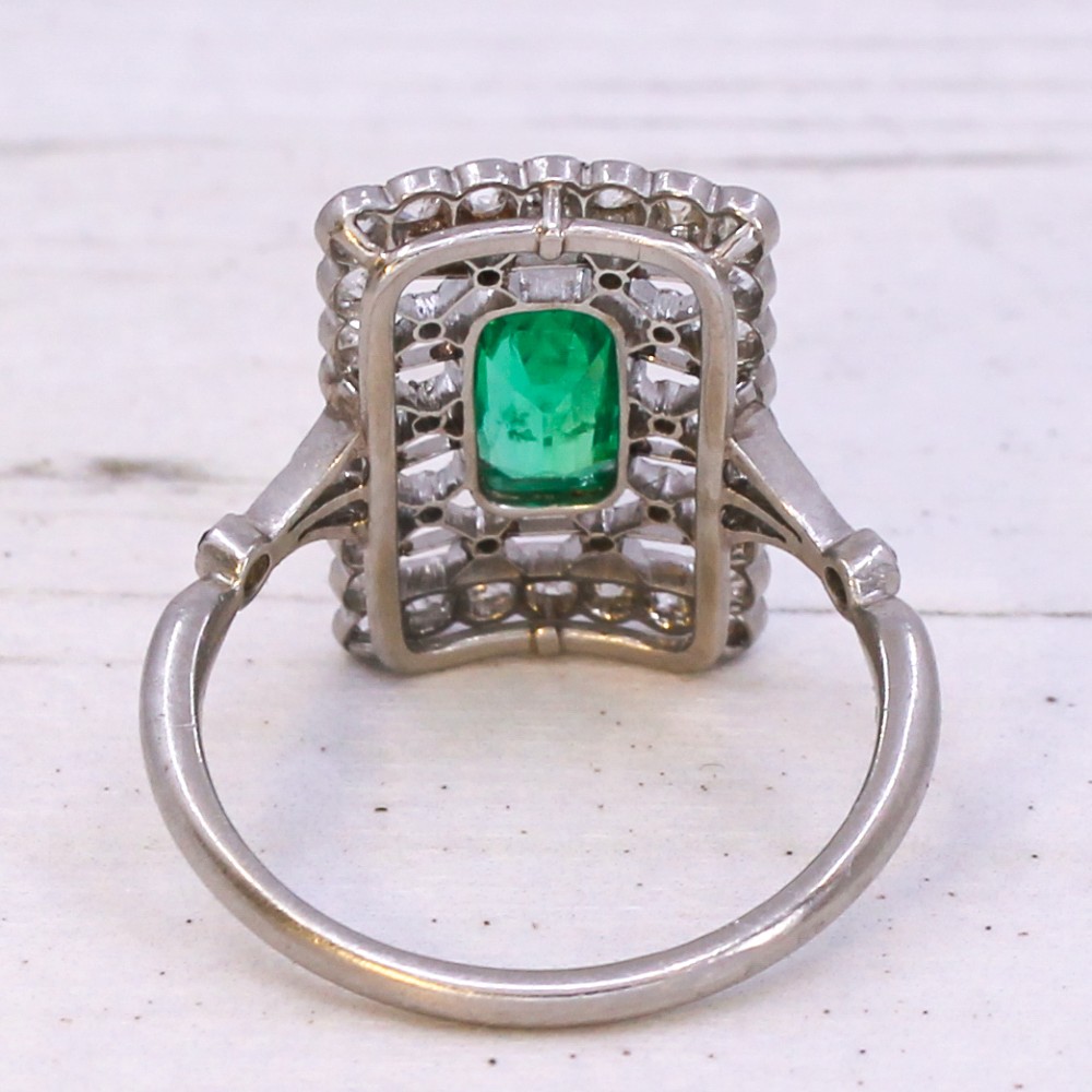 An Edwardian rectangular platinum ring set with a central emerald-cut green gemstone framed by openwork filigree and a diamond border. View V