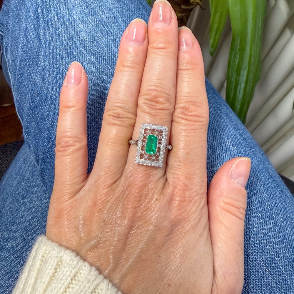 An Edwardian rectangular platinum ring set with a central emerald-cut green gemstone framed by openwork filigree and a diamond border. View VI