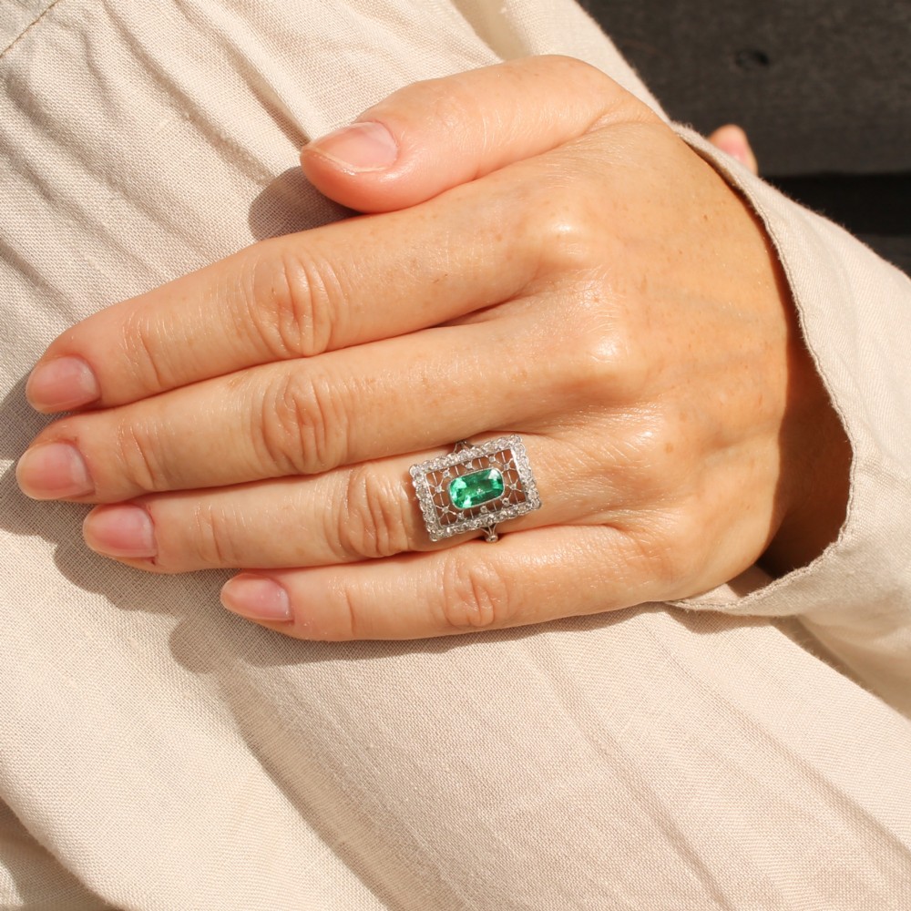 An Edwardian rectangular platinum ring set with a central emerald-cut green gemstone framed by openwork filigree and a diamond border. View VII