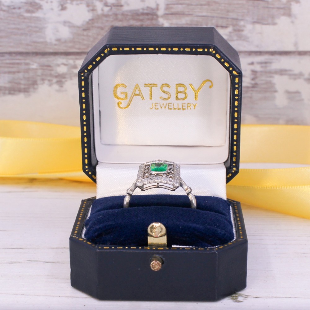 An Edwardian rectangular platinum ring set with a central emerald-cut green gemstone framed by openwork filigree and a diamond border. View IX