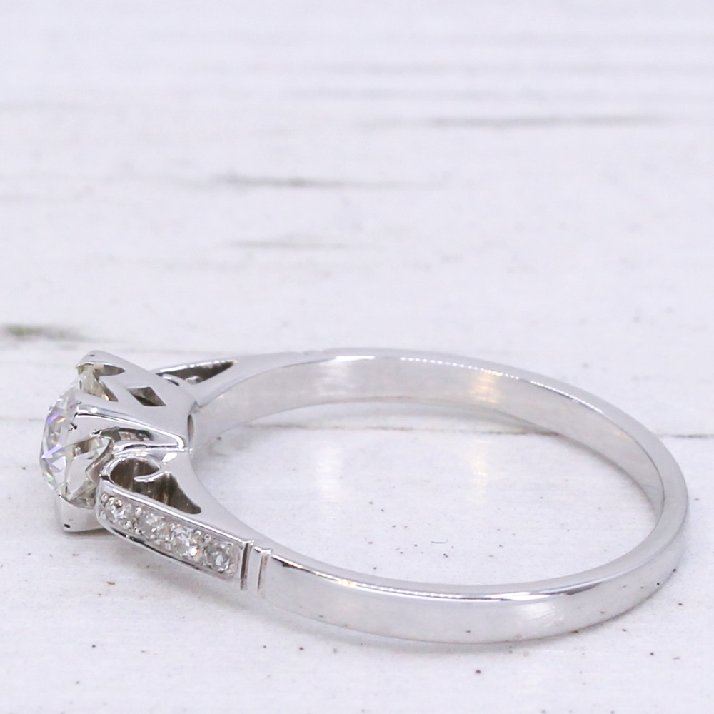 A vintage white metal engagement ring set with a central round old cut diamond flanked by small shoulder diamonds. View IV