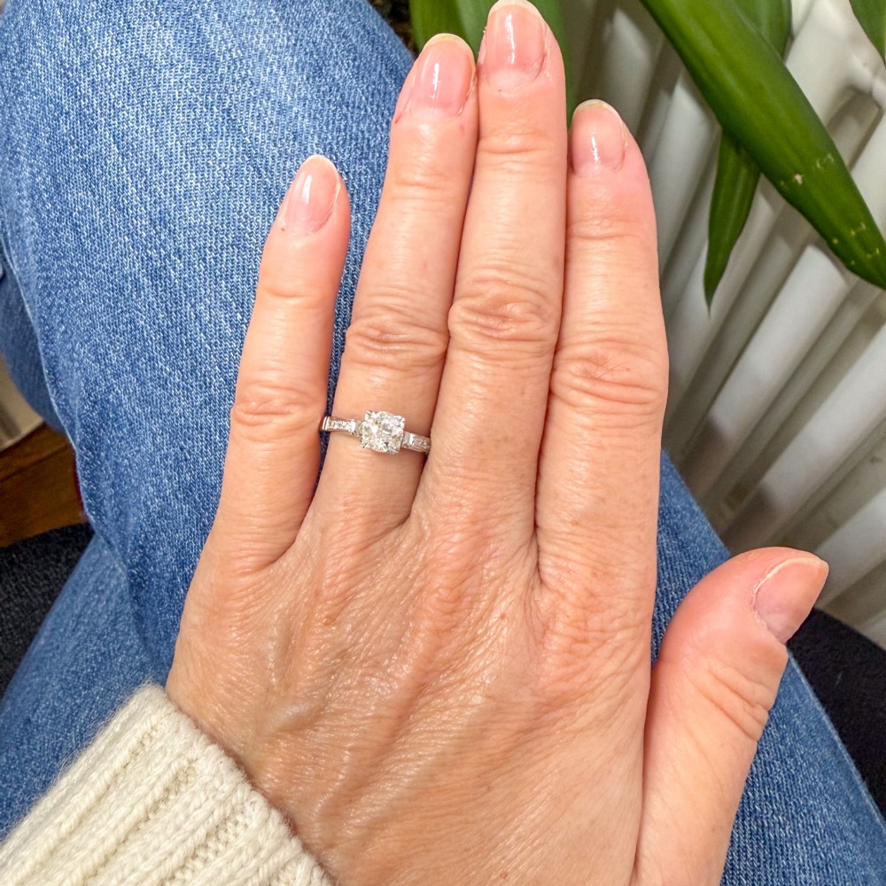 A vintage white metal engagement ring set with a central round old cut diamond flanked by small shoulder diamonds. View VI