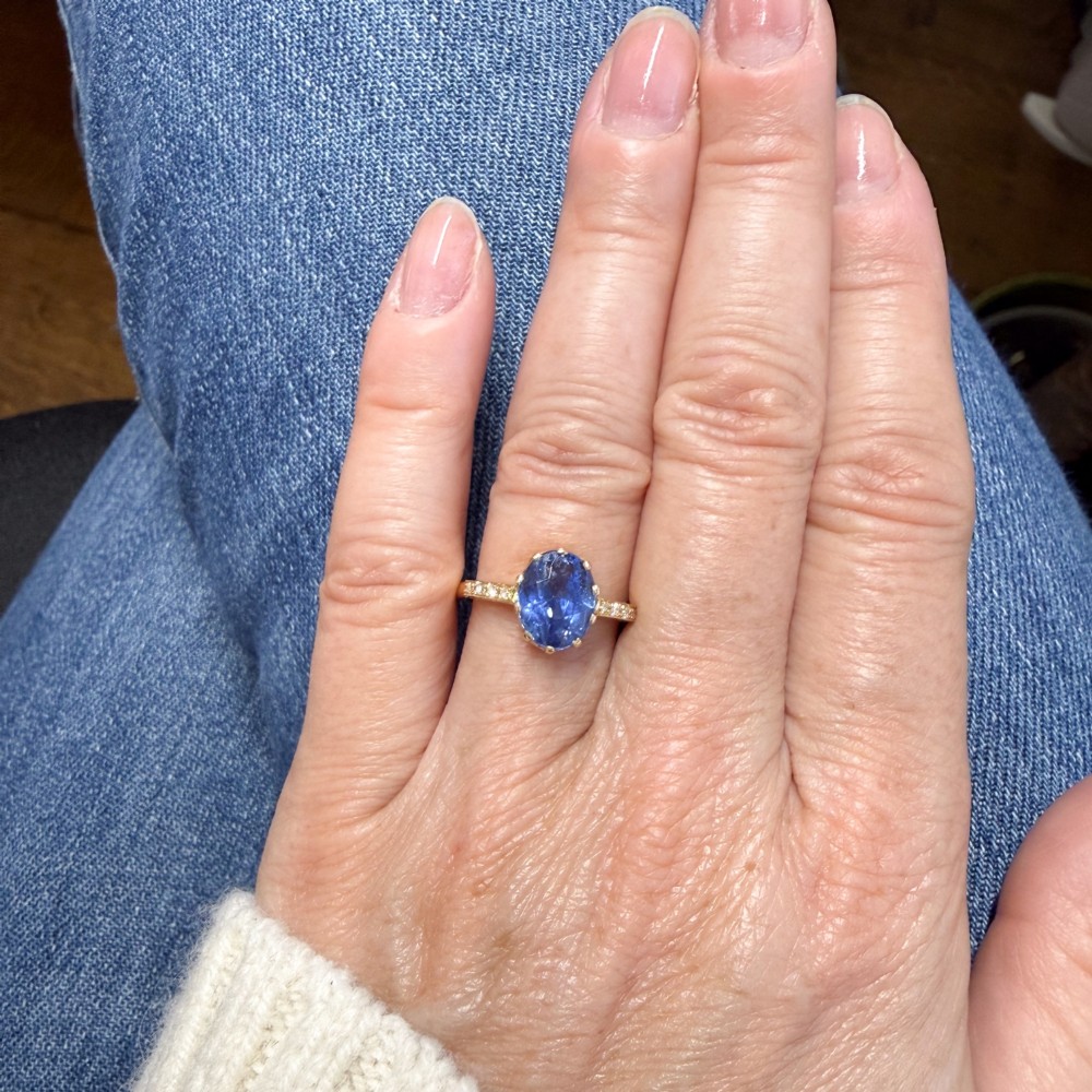 A vintage yellow gold ring featuring an oval-cut blue sapphire in a claw setting with diamond-set shoulders. View VI