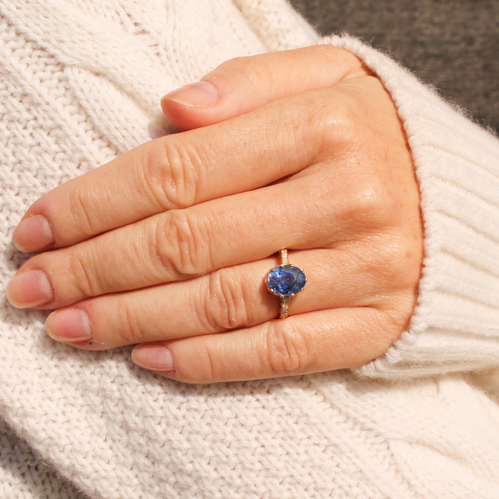A vintage yellow gold ring featuring an oval-cut blue sapphire in a claw setting with diamond-set shoulders. View VII
