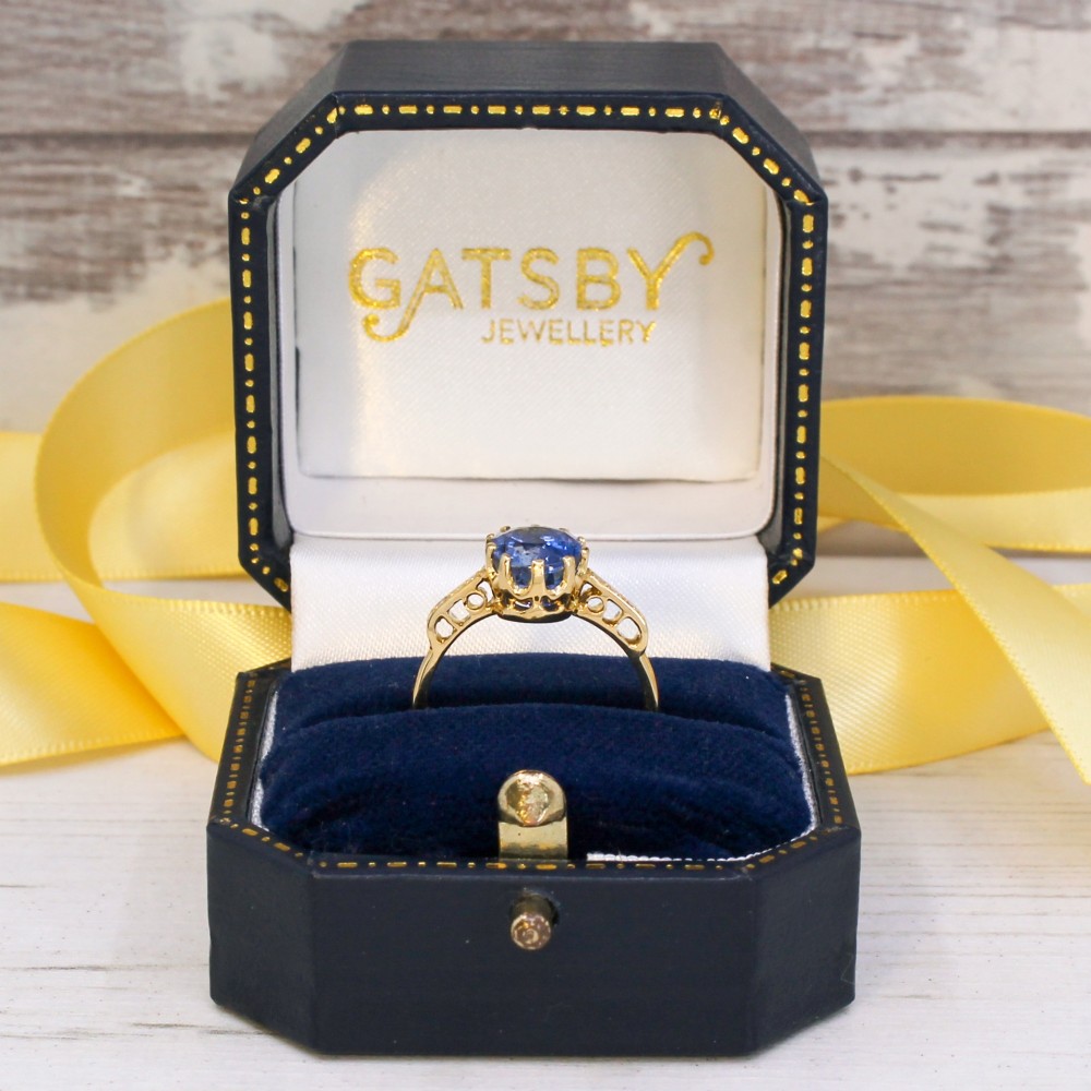 A vintage yellow gold ring featuring an oval-cut blue sapphire in a claw setting with diamond-set shoulders. View IX