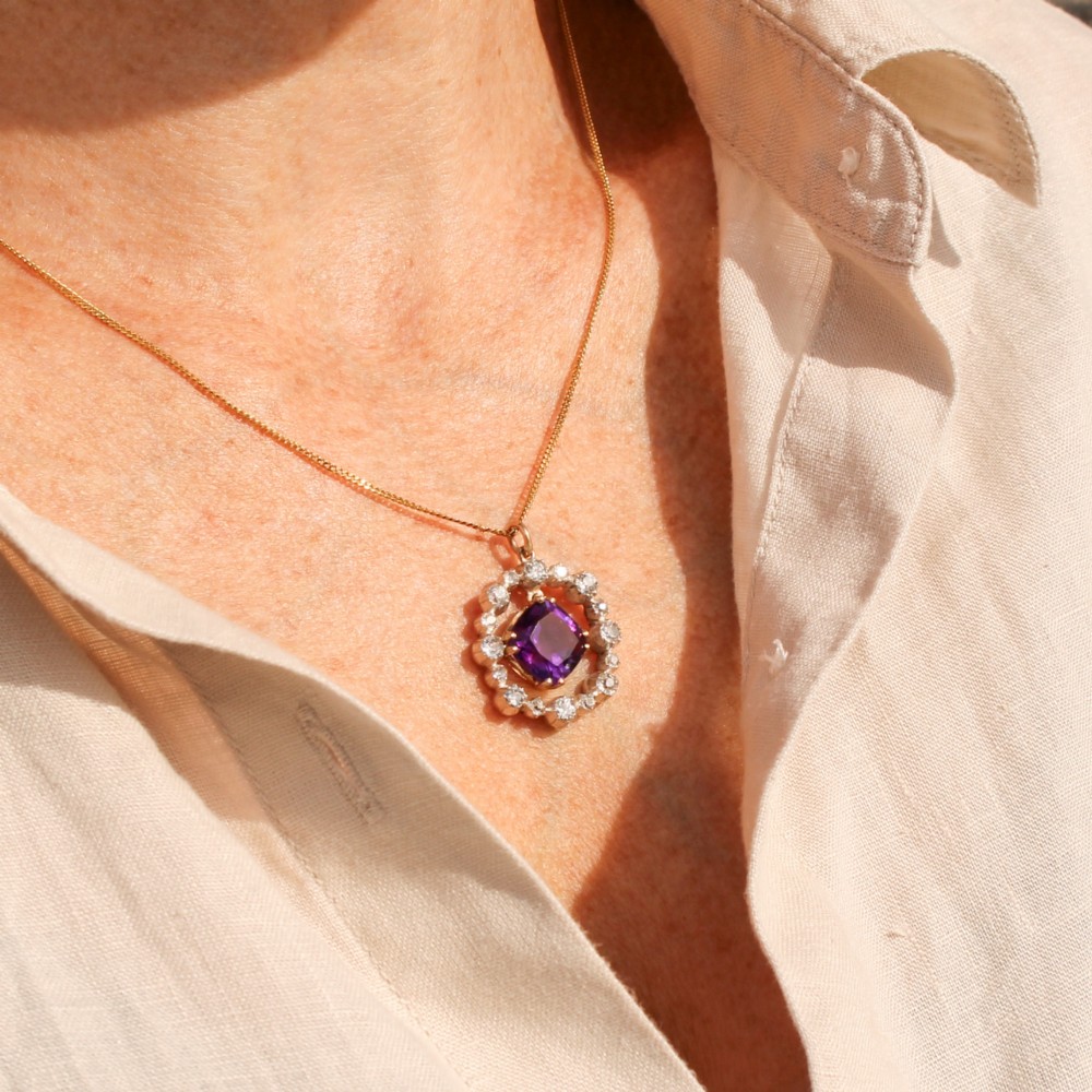 An antique yellow gold pendant featuring a central cushion-cut purple amethyst encircled by an openwork gold border and a halo of old-cut diamonds. View IV