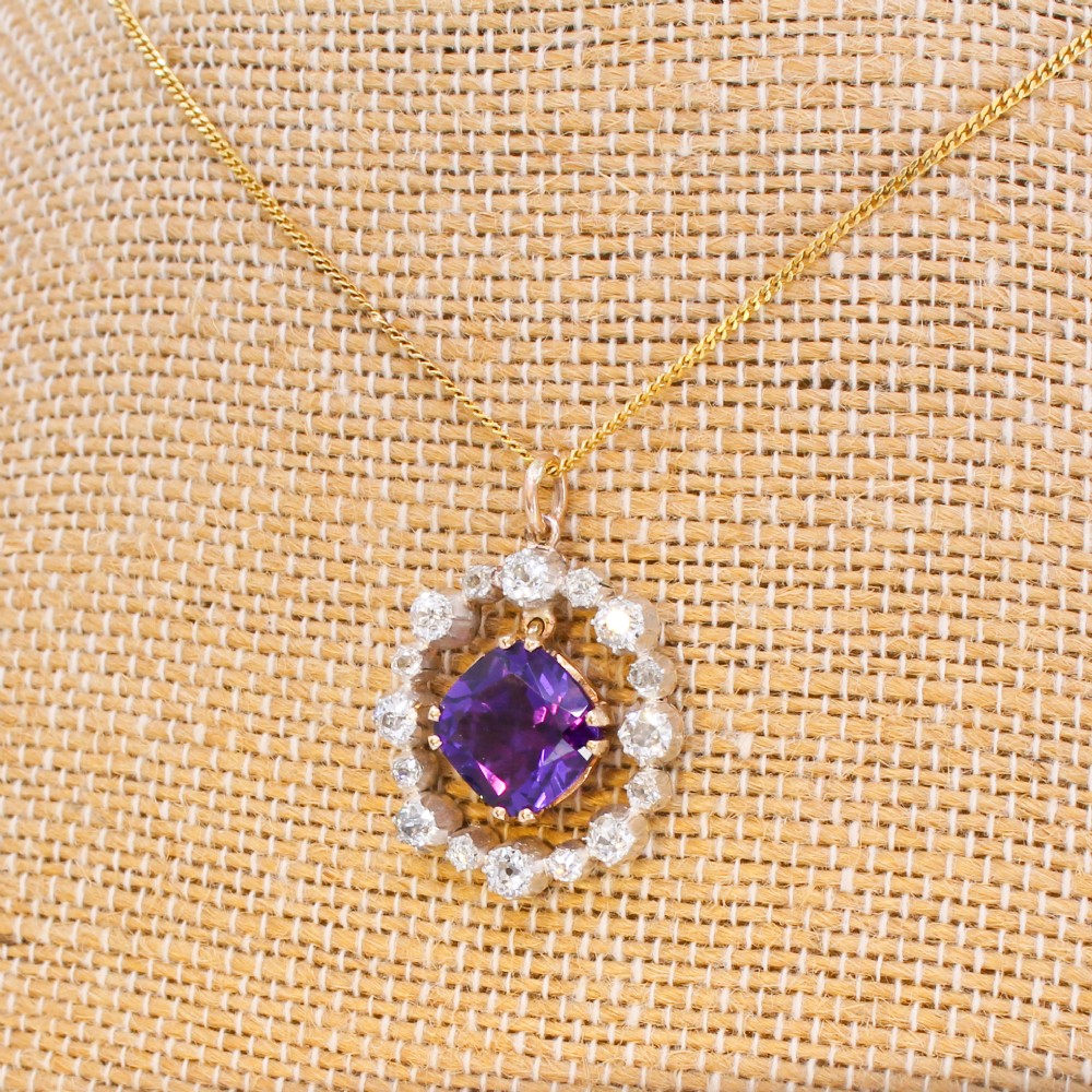 An antique yellow gold pendant featuring a central cushion-cut purple amethyst encircled by an openwork gold border and a halo of old-cut diamonds. View X