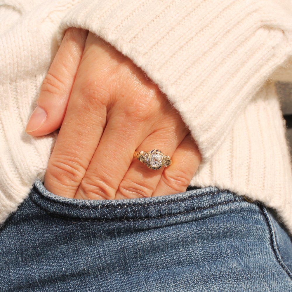 A Victorian yellow gold solitaire ring featuring a central old cut diamond surrounded by blue enamel scrollwork and accent diamonds. View II