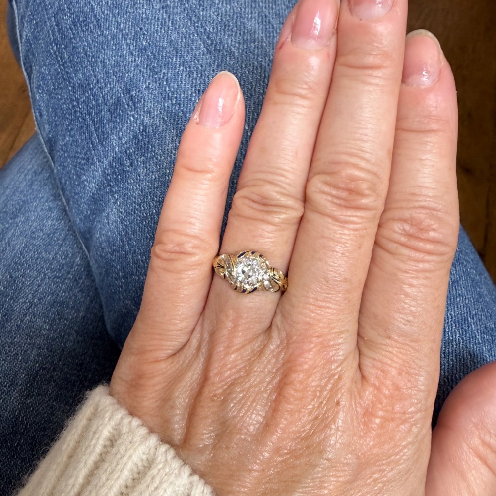 A Victorian yellow gold solitaire ring featuring a central old cut diamond surrounded by blue enamel scrollwork and accent diamonds. View VI