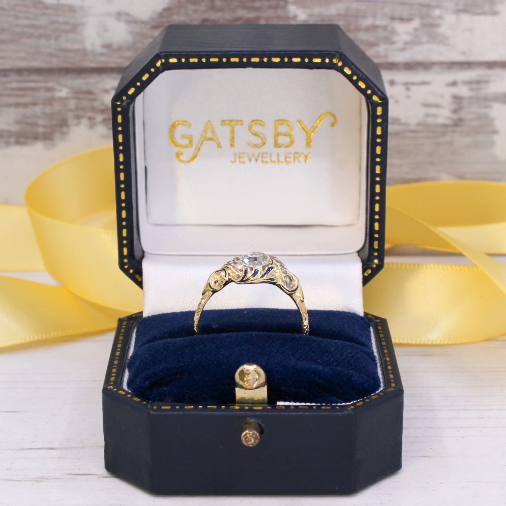 A Victorian yellow gold solitaire ring featuring a central old cut diamond surrounded by blue enamel scrollwork and accent diamonds. View IX