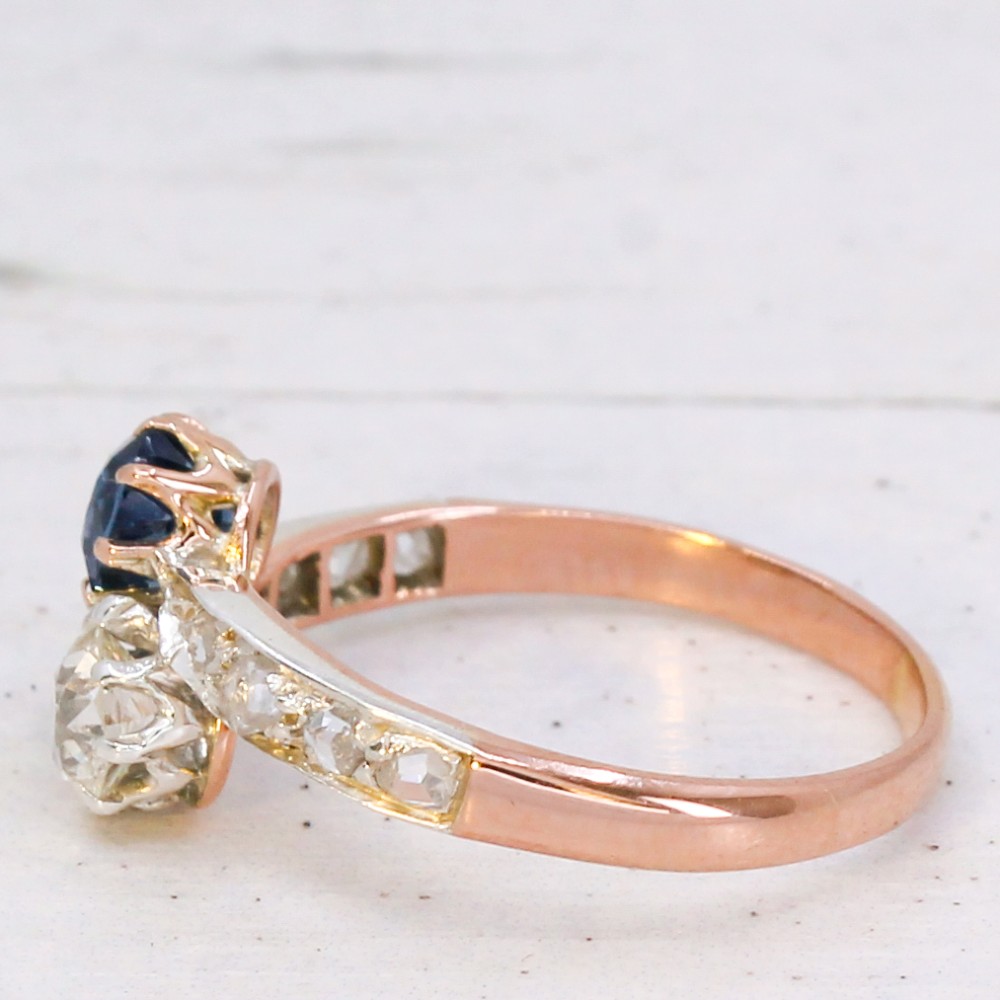 An antique Edwardian gold and platinum crossover ring set with a round blue sapphire and a diamond in a Moi et Toi design. View IV
