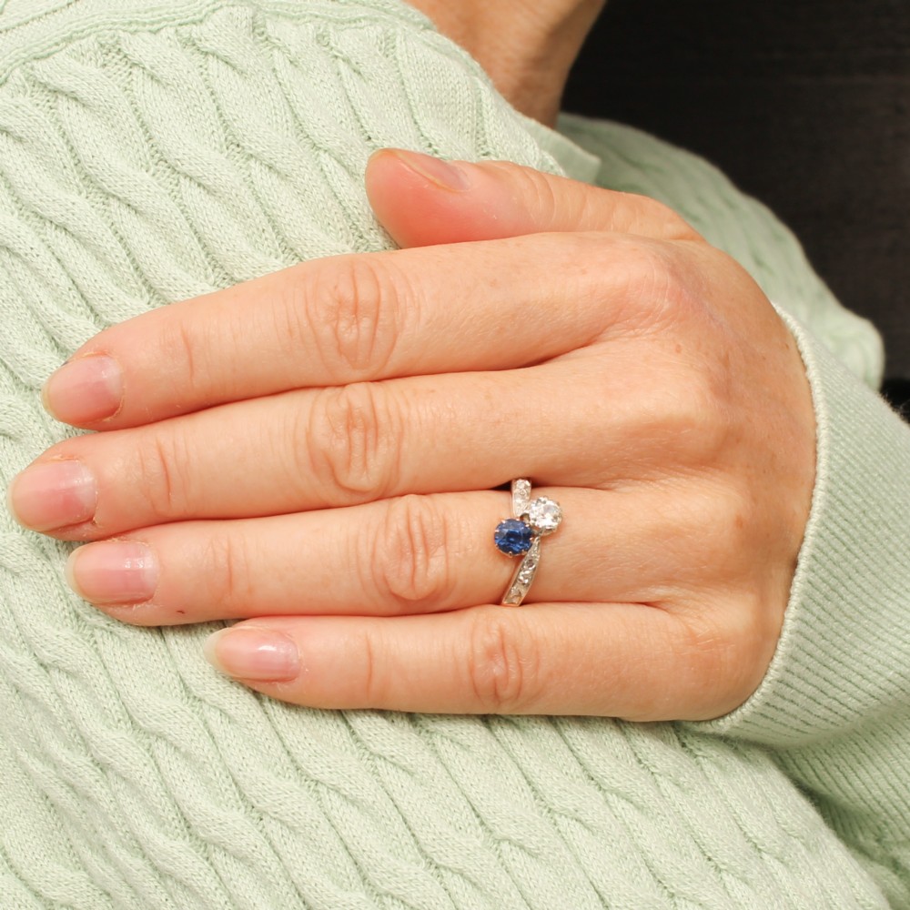 An antique Edwardian gold and platinum crossover ring set with a round blue sapphire and a diamond in a Moi et Toi design. View VI
