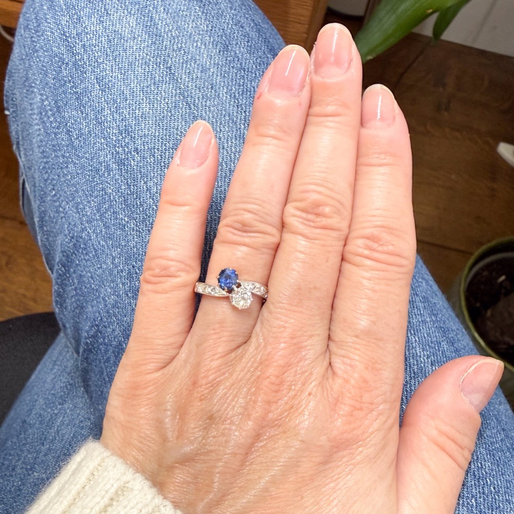 An antique Edwardian gold and platinum crossover ring set with a round blue sapphire and a diamond in a Moi et Toi design. View VII